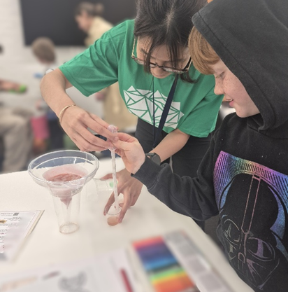 A volunteer in a green Festival t-shirt and child, using a pipette in their experiment.